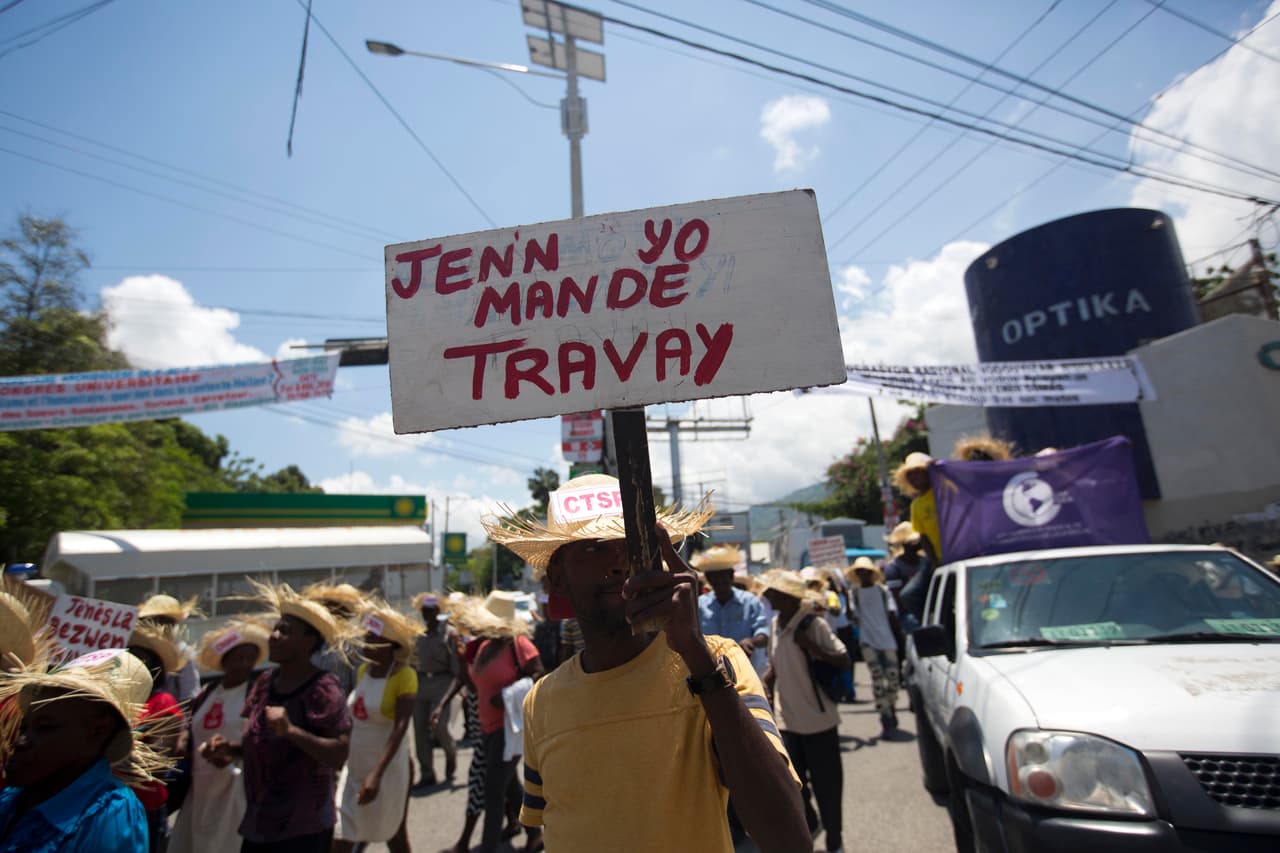 Un hombre sostiene una pancarta que dice en creole "Los jóvenes piden trabajo", mientras que marchan por mejores condiciones de trabajo, durante la marcha del Primero de Mayo en Puerto Príncipe, Haití.