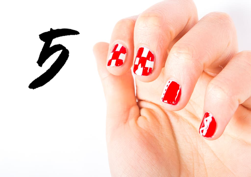 Aplica 2 capas de blanco en la uña del dedo índice y del medio. Y 2 capas de rojo en el meñique y el pulgar. Pinta de rojo la mitad de la uña del anular y de blanco el resto. En el meñique traza un zigzag con el blanco. En el dedo anular traza una línea vertical y decora con puntitos. En el pulgar traza una línea diagonal en blanco. Para el ajedrez usa un pincel #00 y traza líneas verticales y después horizontales haciendo cuadros y rellena.