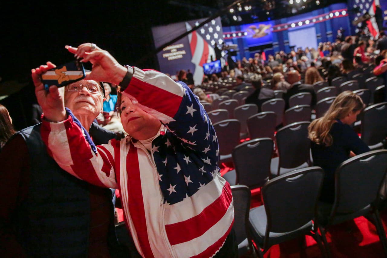 Elizabeth Bartz y su padre Jim Bartz, de Ohio, asistententes al encuentro entre los candidatos presidenciales, se toman una selfie con el escenario de fondo.