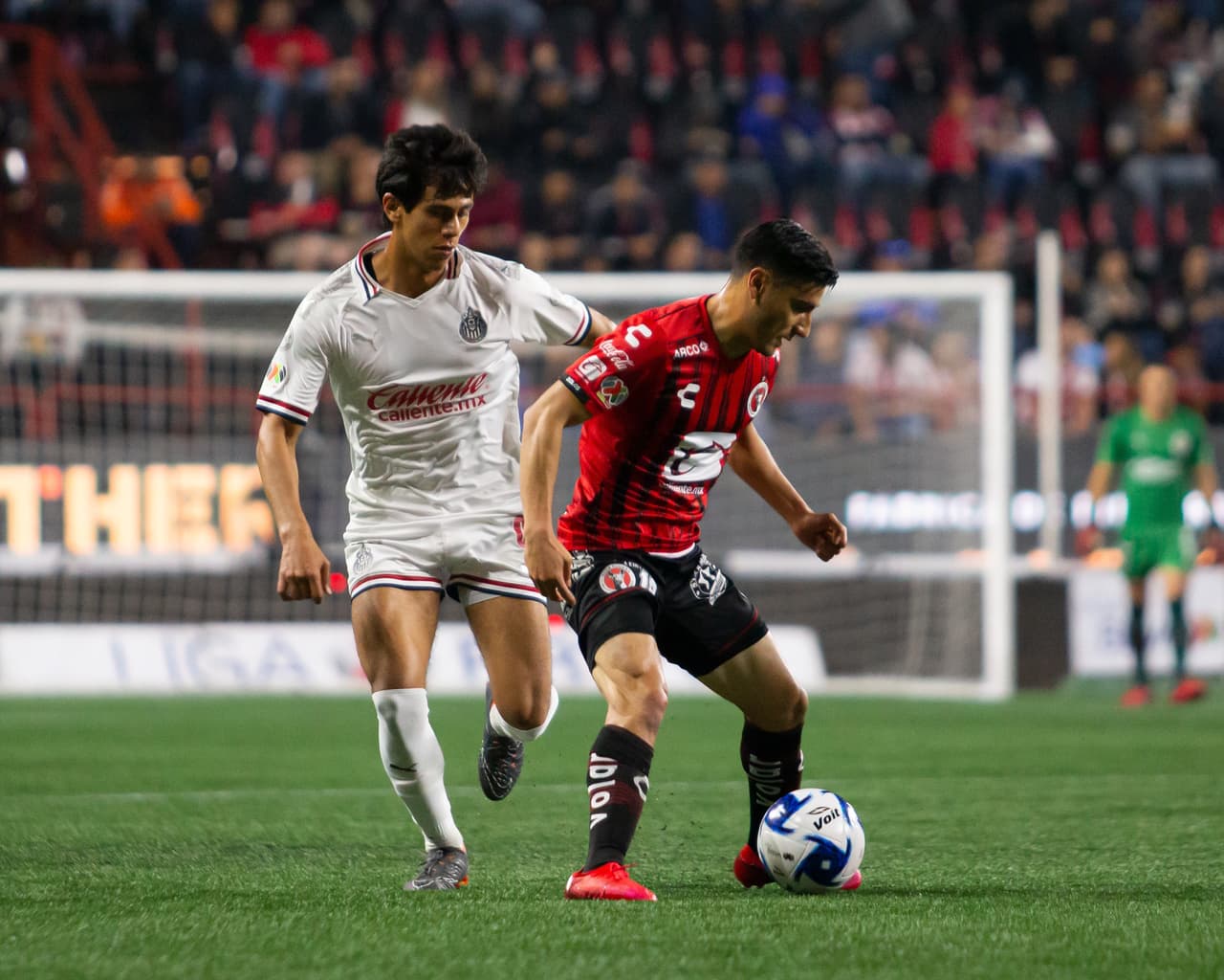 JJ Macías trata de provocar el error en la saga defensiva pero Aldo Cruz no quiere problemas y revienta la pelota.