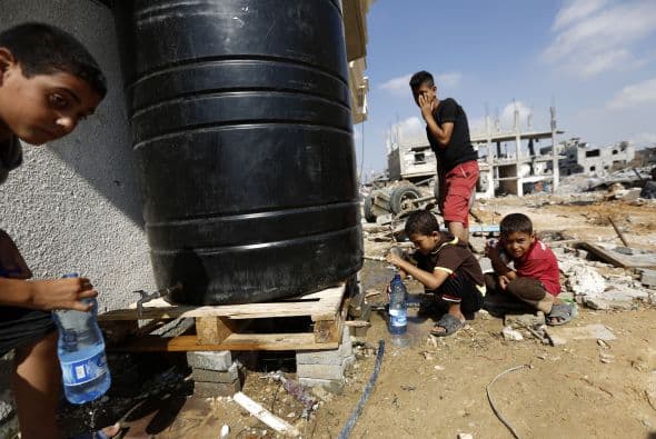 Niños palestinos llenans sus botellas de agua al regresar a su casa destruida en la ciudad de Beit Hanun, al norte de Gaza.