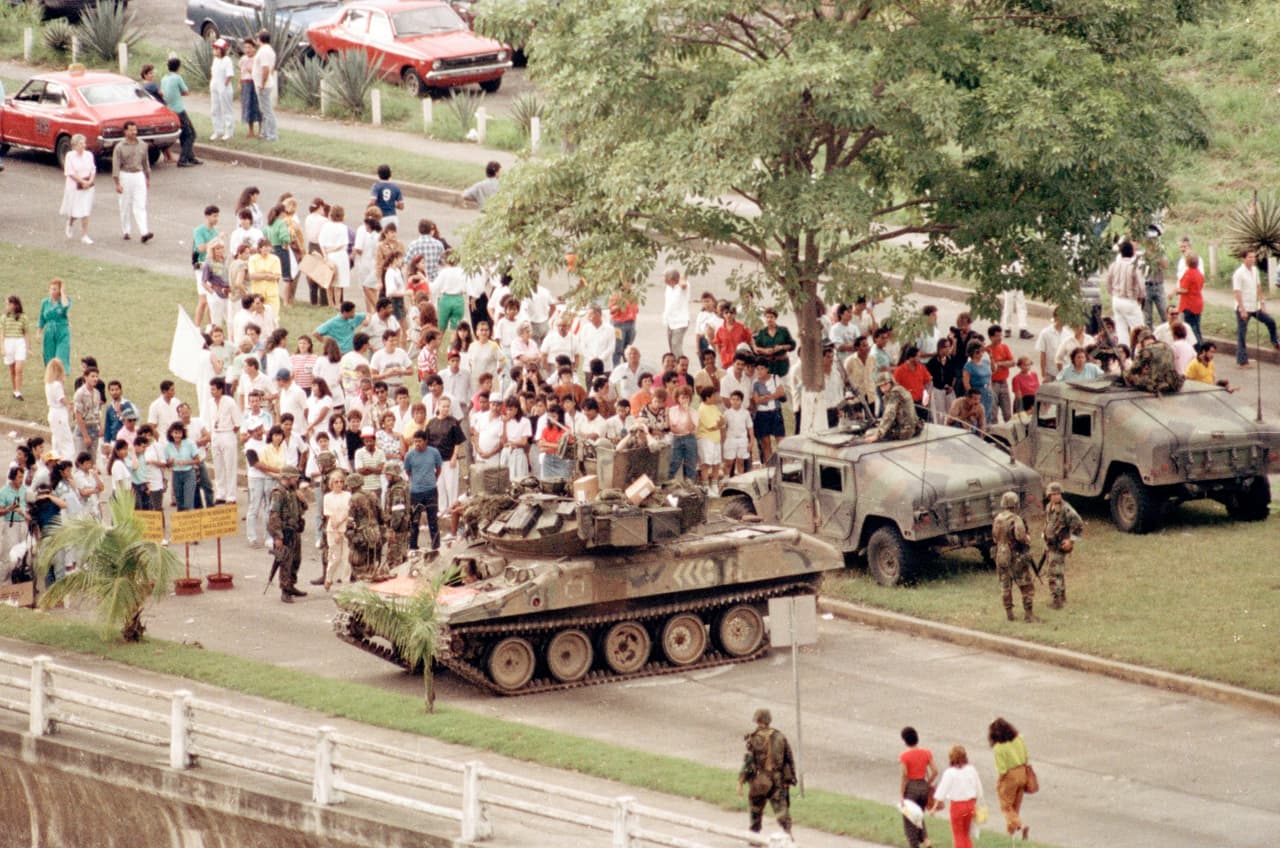 U.S. Army armored vehicles form a blockage on Panama City's Balboa Avenue, leading towards the Vatican Embassy Wednesday, Dec. 27, 1989 where Manuel Noriega has sought refuge. A crowd of Anti-Noriega demonstrators gather around the tanks.