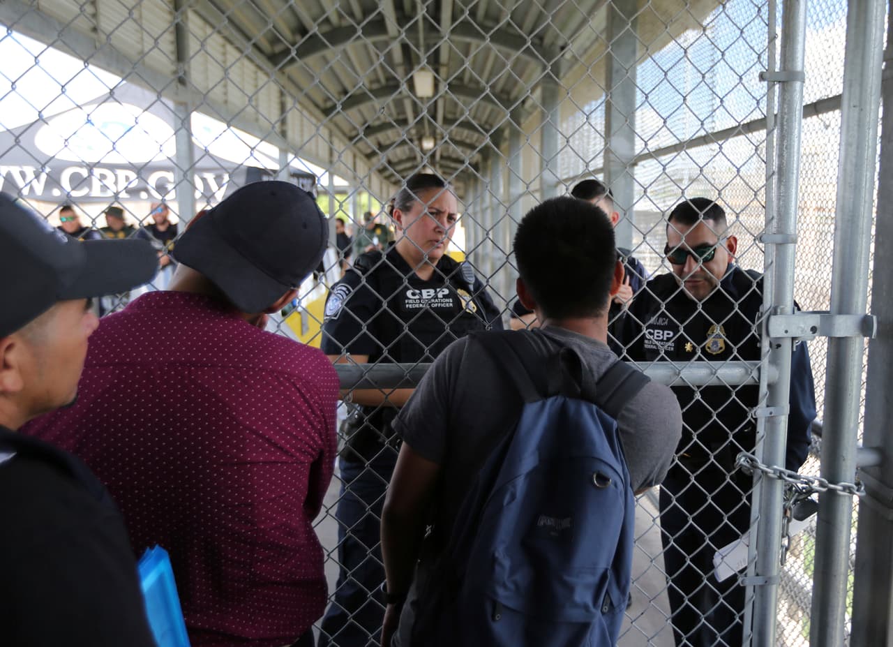 Los migrantes consultando a los agentes de CBP sobre la reapertura del Puente Internacional Gateway. Muchos de los solicitantes de asilo que han sido enviados a México viven en tiendas de campaña o en las aceras al final del puente, dependen de alimentos de voluntarios y se asean con agua del río. Dijeron recientemente a la agencia Reuters que estaban preocupados porque sus citas en la corte fueran canceladas o pospuestas indefinidamente.
<br>