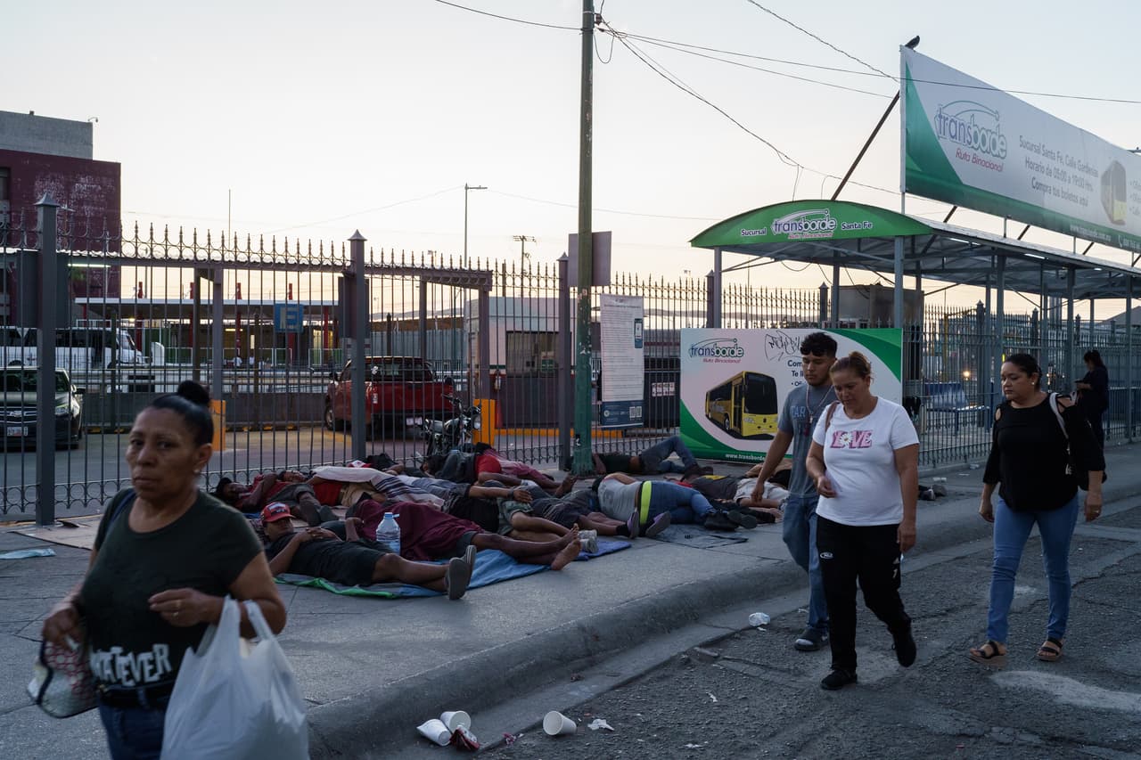 Habitantes locales pasan caminando mientras inmigrantes, muchos de ellos venezolanos, duermen en la entrada de un puente internacional que separa a Ciudad Juárez, México, de la ciudad de El Paso, Texas. Algunos de los inmigrantes esperan en la ciudad fronteriza mientras intentan conseguir una cita para entrar a Estados Unidos usando la aplicación gubernamental CBP One.