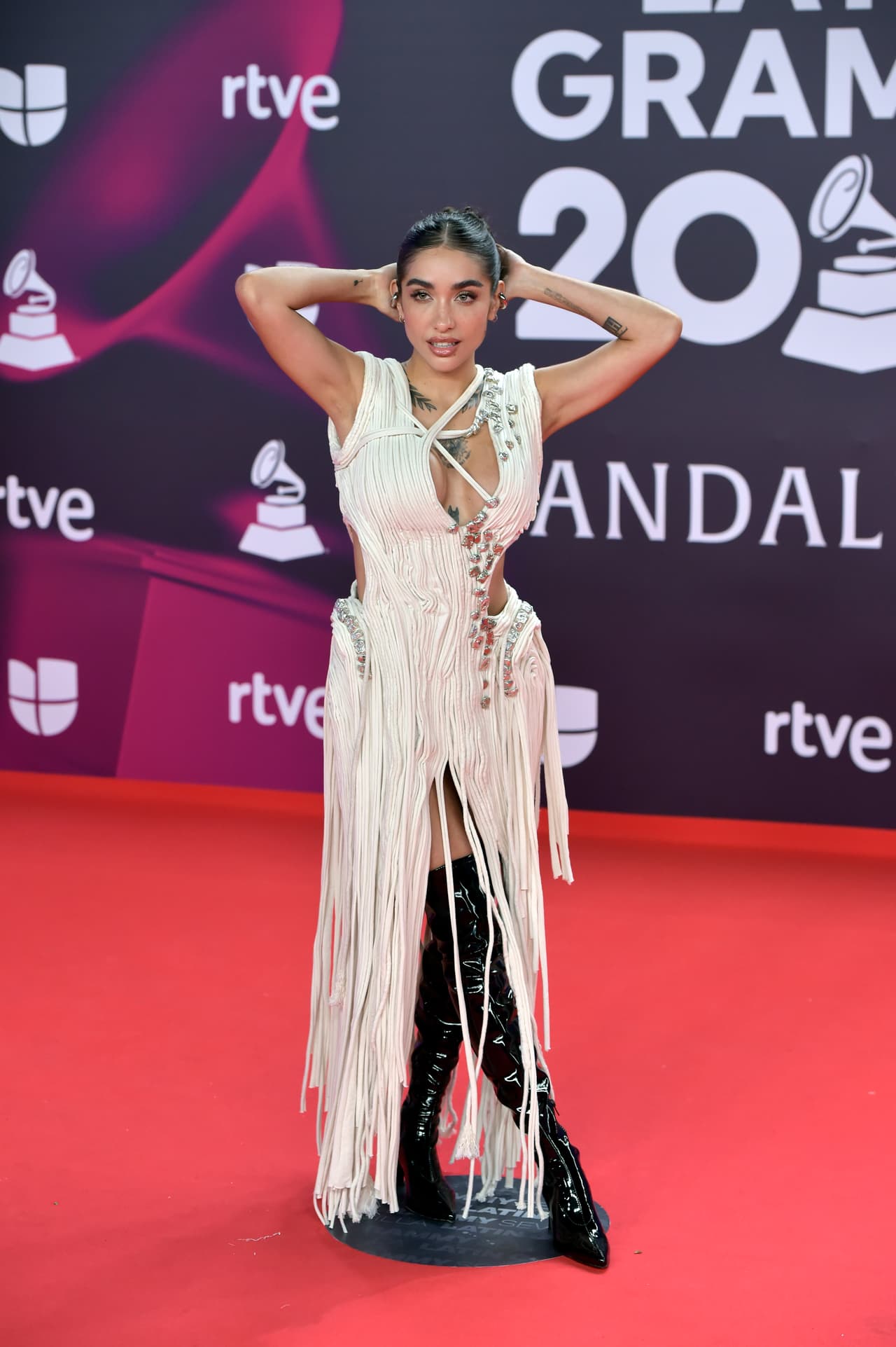 <b>Maria Becerra </b>combinó un vestido blanco de lazos con un par de botas altas y negras.