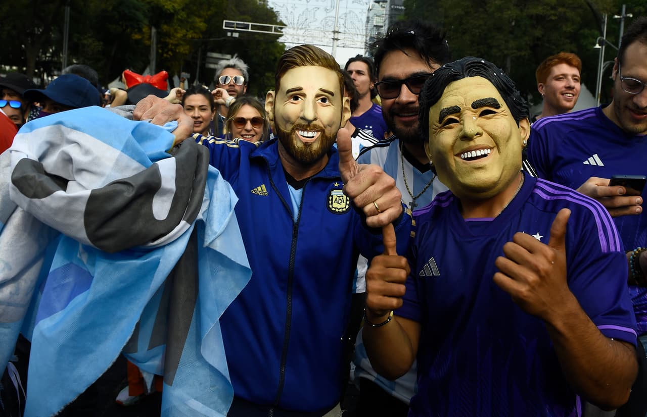 Hinchas de la selección argentina celebran en las calles de la Ciudad de México este domingo. Dos de ellos llevan puestas máscaras que asemejan a Lionel Messi y Diego Armando Maradona.