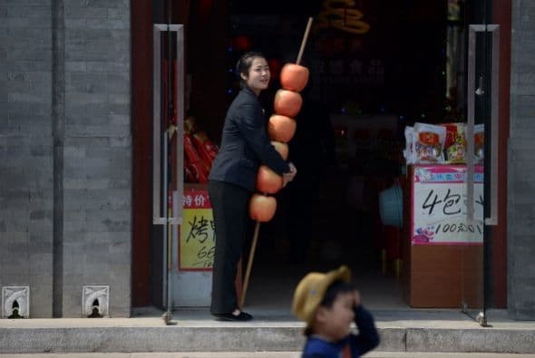 Una mujer sostiene una cadena de manzanas mientras espera clientes en la entrada de su negocio en Beijing.