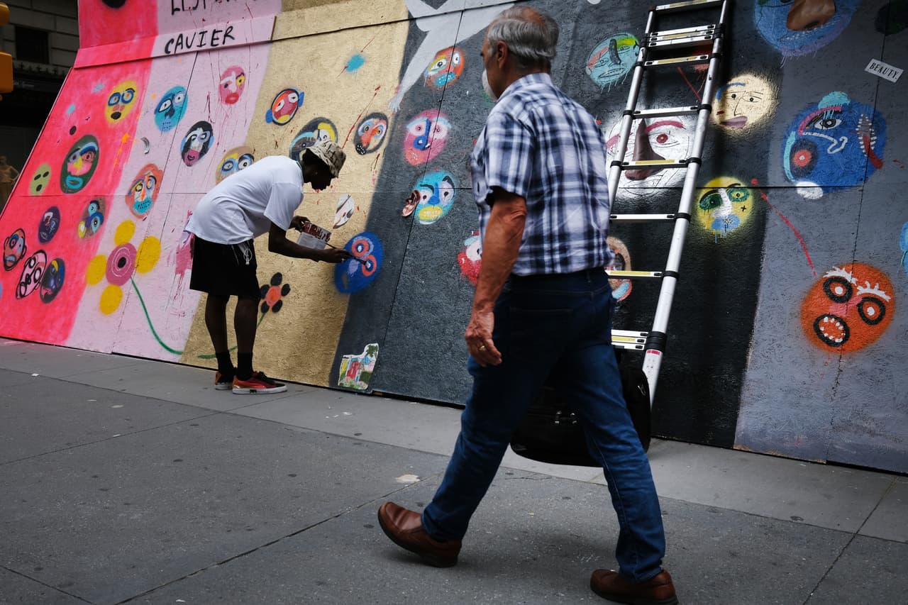 Un artista que se hace llamar Cavier pinta sobre una tienda Puma en Manhattan cuyo frente está cubierto, mientras la ciudad se prepara para entrar en la etapa 2.