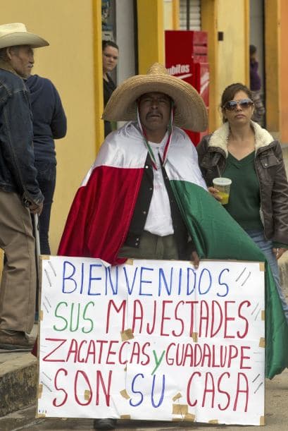 Un hombre sostiene un cartel que dice "Bienvenido Sus Majestades. Zacatecas y Guadalupe son de su casa.