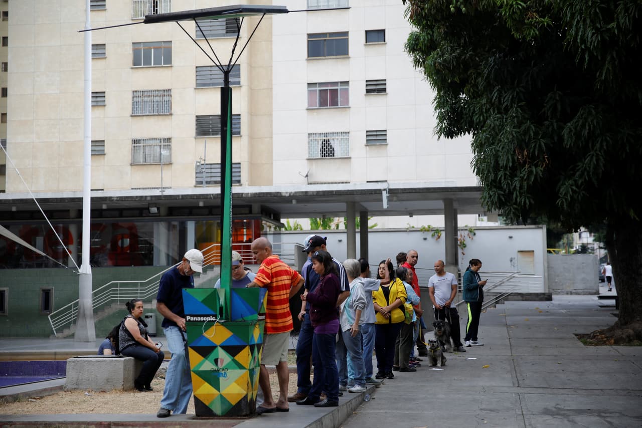 Personas forman una cola esperando el turno para poder regarcar su teléfonos celulares en una plaza pública en el este de Caracas.