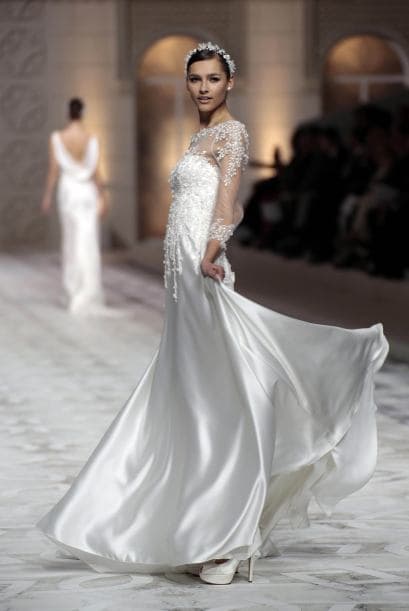 Telas satinadas, un escote sencillo pero cubierto con transparencias y un tono marfil le dan el estilo clásico a este vestido.