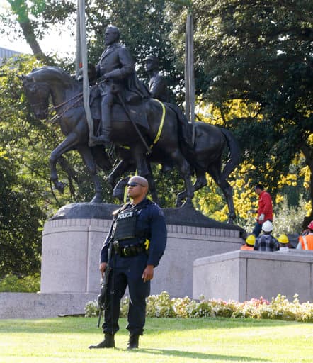 Un policía vigila el área mientras trabajadores remueven la estatua del general Lee.