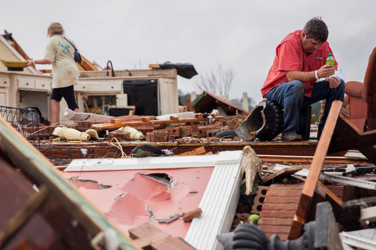 Jeff Bullard se sienta en lo que solía ser el vestíbulo de su casa, mientras su hija, Jenny Bullard, mira a través de escombros en su casa que fue dañado por un tornado, en Adel, Georgia.