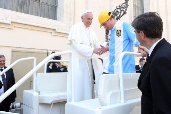 Este pequeño vestido con la playera del equipo de futbol argentino da la mano al Papa.