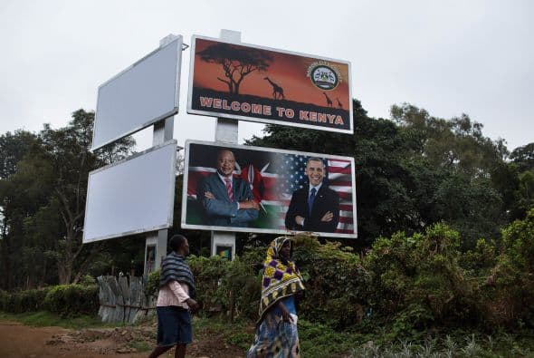 Peatones caminan bajo un enorme cartel con los presidentes Obama y Kenyatta.