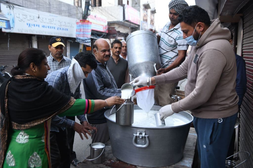 Gente comprando leche en una calle de una ciudad india.