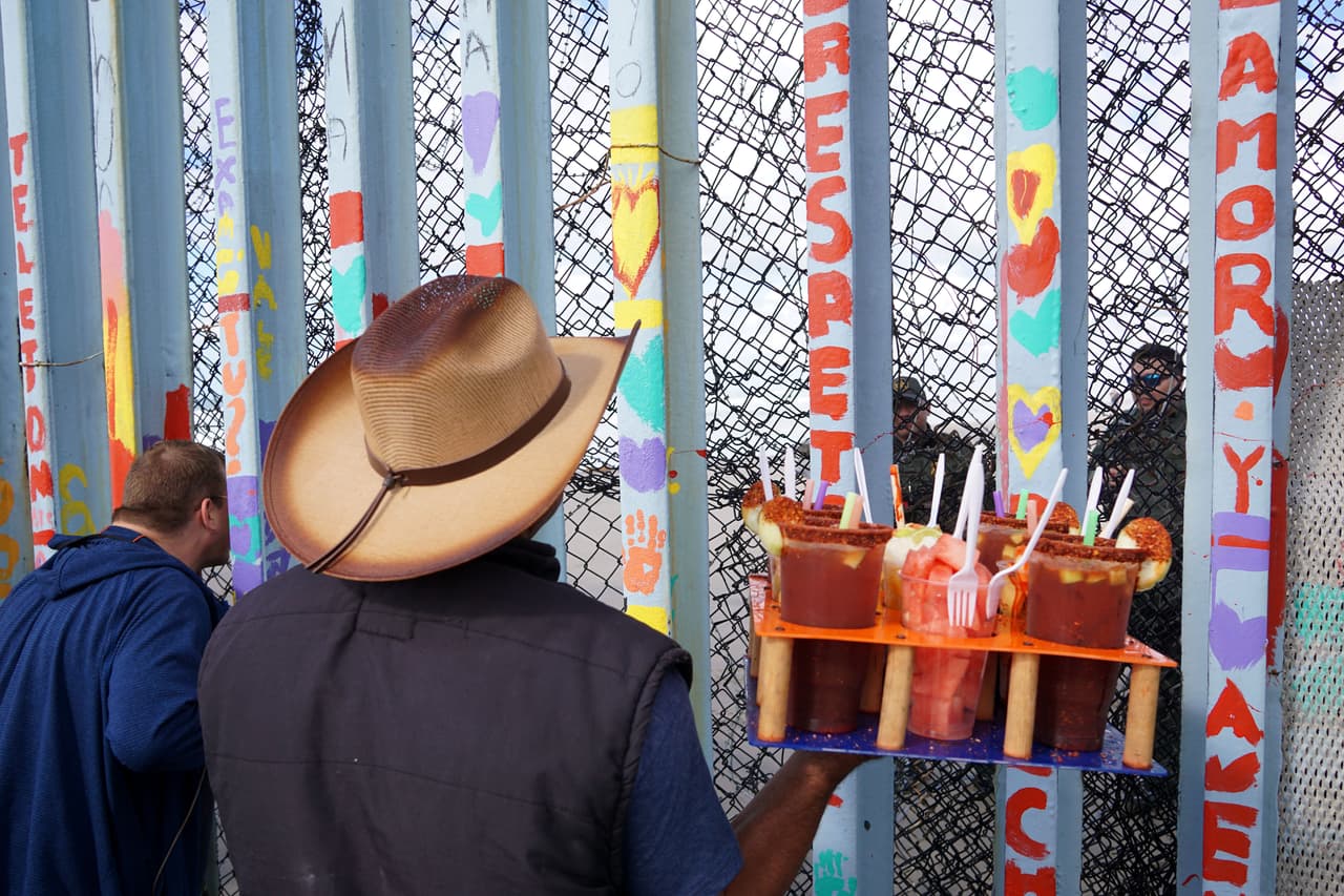 <b>Micheladas para la Patrulla Fronteriza.</b> Un vendedor ambulante de la playa de Tijuana conversa con los agentes de la Patrulla Fronteriza estadounidense a través de la valla limítrofe. Esta zona del límite entre EEUU y México se ha convertido en un atractivo turístico 
<a href="https://www.univision.com/shows/noticiero-univision/controversia-en-tijuana-porque-varios-visitantes-estan-utilizando-el-muro-fronterizo-como-atraccion-turistica-video">visitado por personas de todo el mundo</a>.