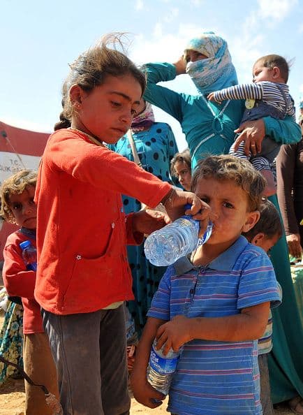 Esta niña refugiada ayuda a su hermano a beber agua después del pesado éxodo para llegar a la frontera turco-siria para huir de la amenaza yihadista.