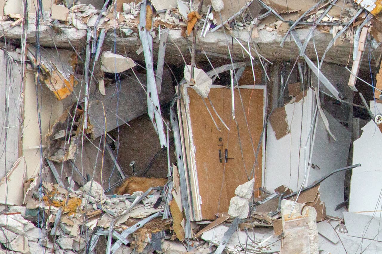 Una lluvia fuerte pero intermitente ha estado acompañando a las autoridades, periodistas y curiosos cerca del edificio 
<a href="https://www.univision.com/noticias/estados-unidos/edificio-12-pisos-colapsa-parcialmente-miami"><b>Champlain Towers South</b></a>. A veces la brisa marina levanta una espesa nube de polvo de los escombros, que a pesar de la lluvia persiste.
<br>
<br>En la playa la policía no molesta a los curiosos. Solo llaman la atención a los osados que traspasan la cinta amarilla para tener una mejor perspectiva.
<br>