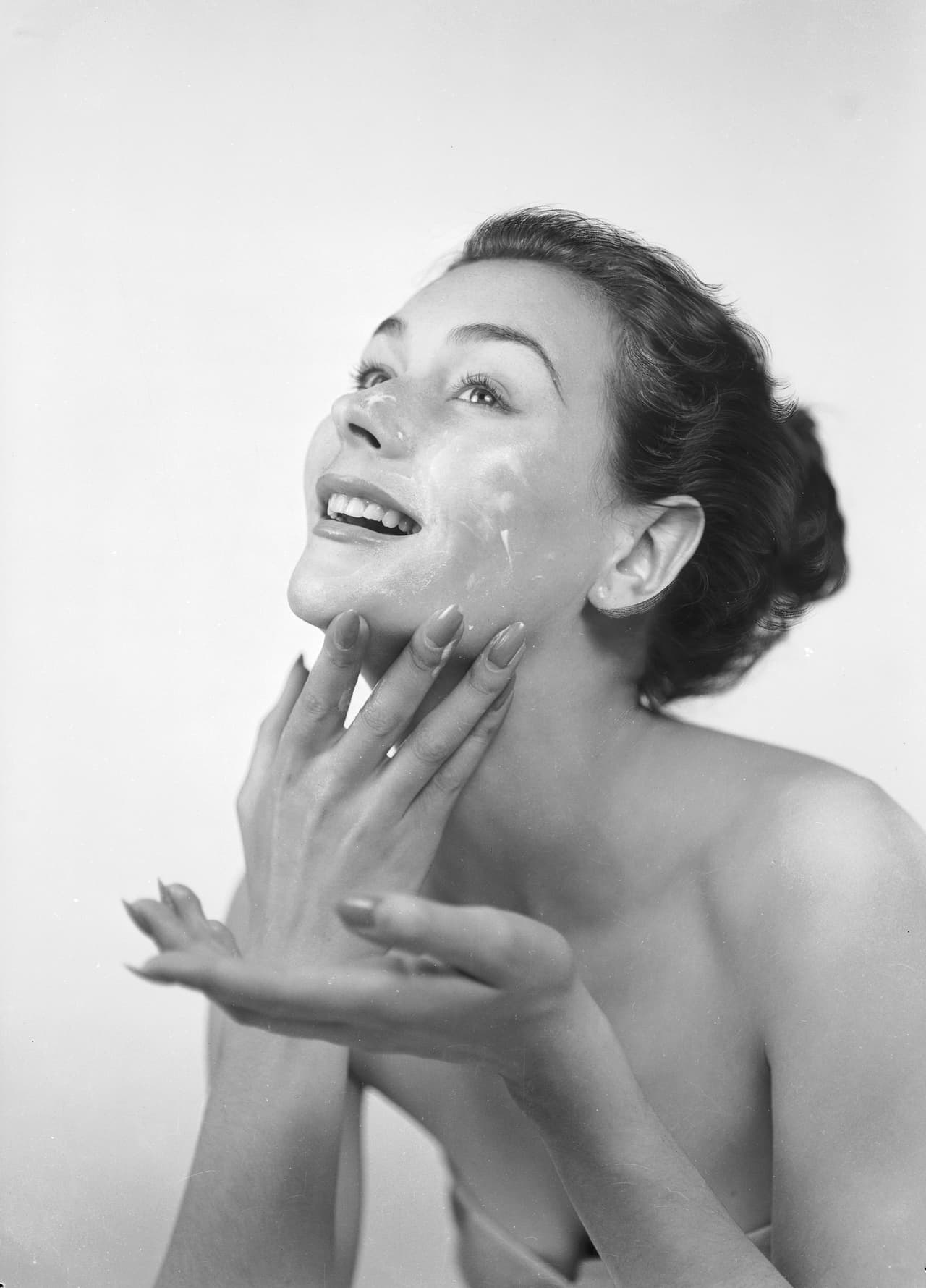 A woman applies cream to her face and neck.