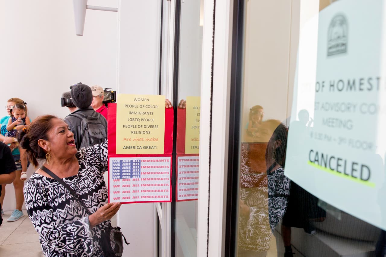 Una manifestante se acerca a la puerta de la alcaldía de Homestead, en Florida. Pedía ser atendida por alguna autoridad a la que reclamarle que se cumplan los derechos de las personas indocumentadas con un cartel en el que se lee en inglés: “Mujeres, gente de color, inmigrantes, personas LGBTQ, gente de distintas religiones, son lo que hacen a América grande”.