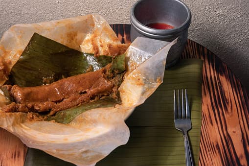 La hoja de la planta del guineo, debidamente amortiguada, cubría su entorno para su cocción y el amarre original utilizado fue el hollejo o fibra de las plantas del guineo o plátano. Es el llamado pastel de masa.