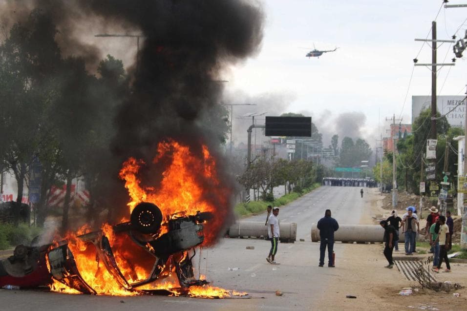 Teachers blocking a federal highway hold their positions next to a burning car