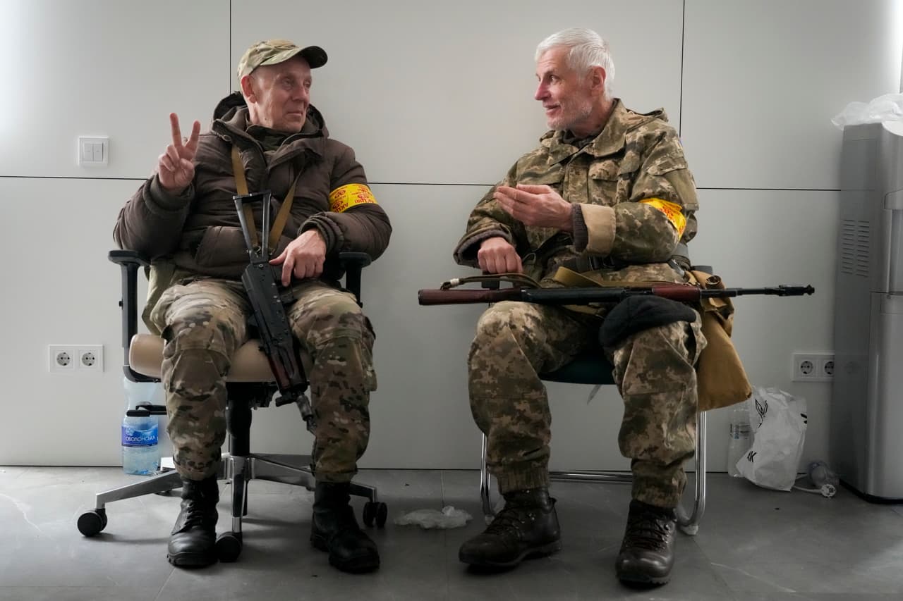 Dos civiles armados conversan cerca del ayuntamiento de Kiev este domingo 27 de febrero de 2022. 
<b>Las recién entrenadas fuerzas de defensa civil montaban guardia en puestos de control de la capital y patrullaban las calles vacías.</b>