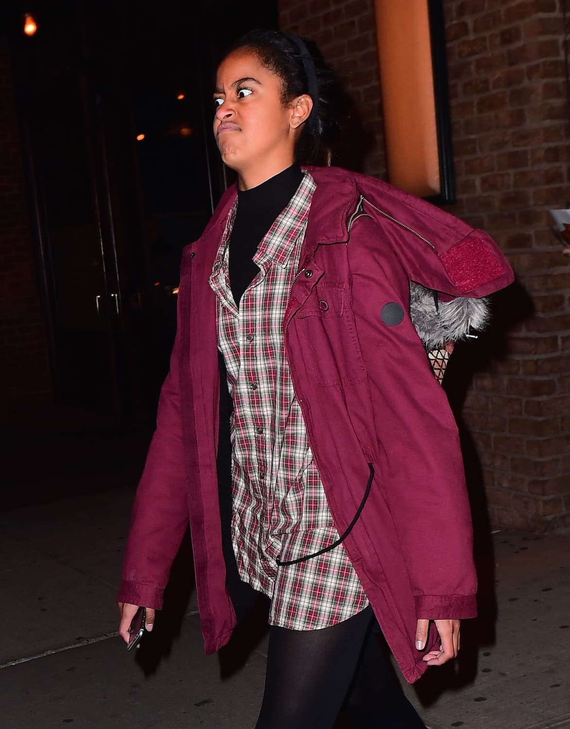 Malia Obama, un poco cansada de los paparazzis, luce un abrigo marrón, camisa a cuadros y su pelo cogido.