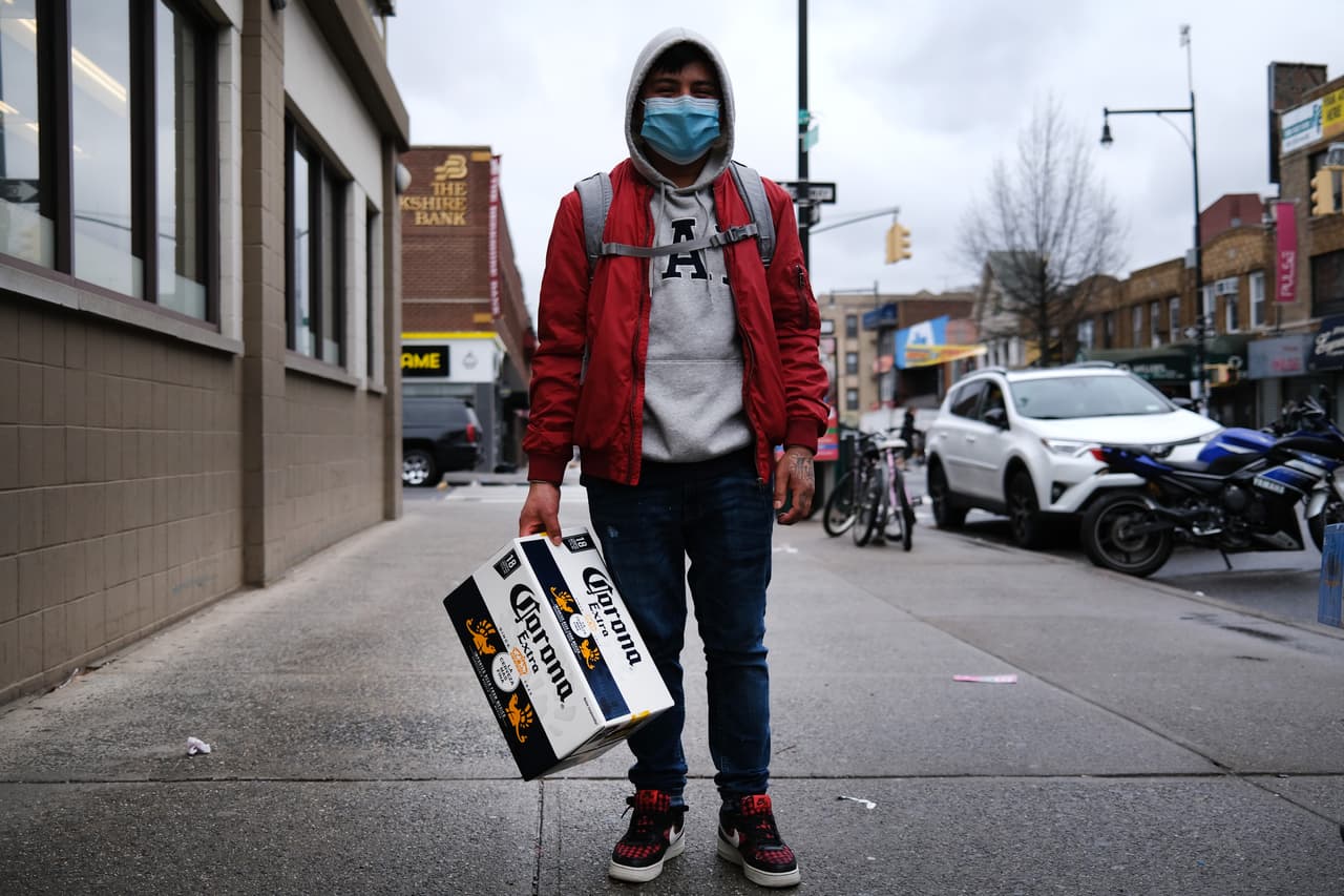 <b>Necesidades esenciales y más. </b>Un hombre protegido con una máscara lleva un empaque de cervezas en Brooklyn, donde los comercios no esenciales permanecen cerrados. En este y otros estados con restricciones la venta de licor no ha sido suspendida.