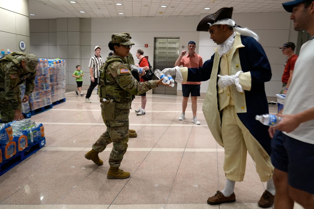 Personal militar reparte agua a la gente que busca refugio en el Edificio Federal Ronald Reagan tras evacuar el National Mall debido al mal tiempo, durante los actos conmemorativos del 250 aniversario de la independencia de la nación, el sábado 4 de julio de 2026, en Washington.