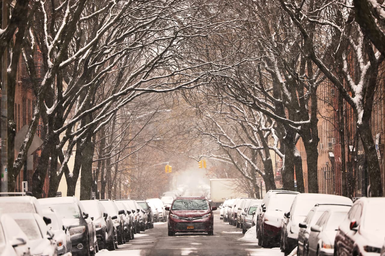 Un coche circula por una calle nevada de Brooklyn
