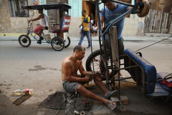 Usando herramientas rudimentarias, un mecánico trata de reemplazar una rueda de un bicitaxi.