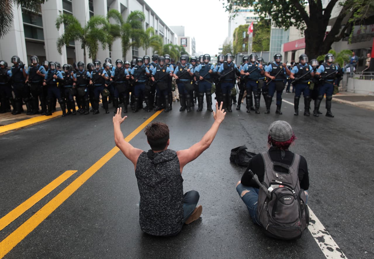 Dos manifestantes sentados frente al contingente policial que fue apostado en una de las principales avenidas del área metropolitana. (Reuters)
