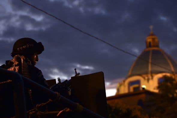 Un miembro de la Unidad Especial Rural que lleva un cinturón de balas 7.62 mm en el cuello resguarda la plaza principal.
