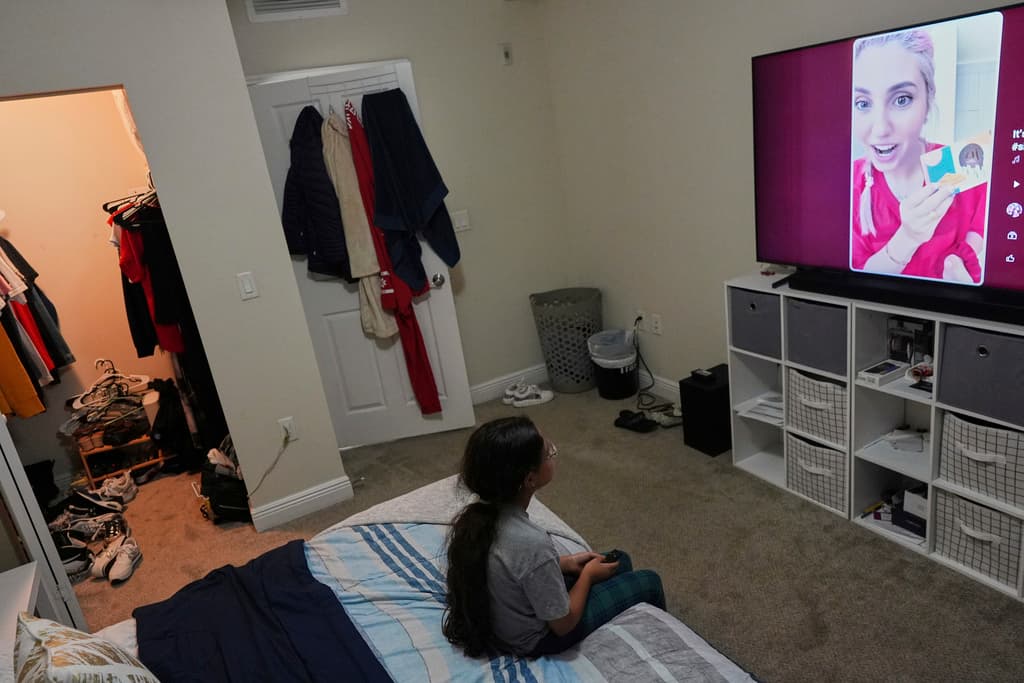 Una niña de 9 años con estatus de protección temporal, o TPS, que nació en Venezuela pero que sólo habla inglés con fluidez y está en el programa de niños con talento de su escuela, ve la televisión en el apartamento de su familia, el sábado 5 de abril de 2025, en Doral, Florida. (AP Foto/Rebecca Blackwell)