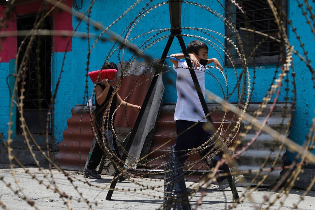 Los niños caminan detrás de una alambrada mientras los soldados vigilan las entradas de la comunidad de San José del Pino en Santa Tecla, El Salvador.