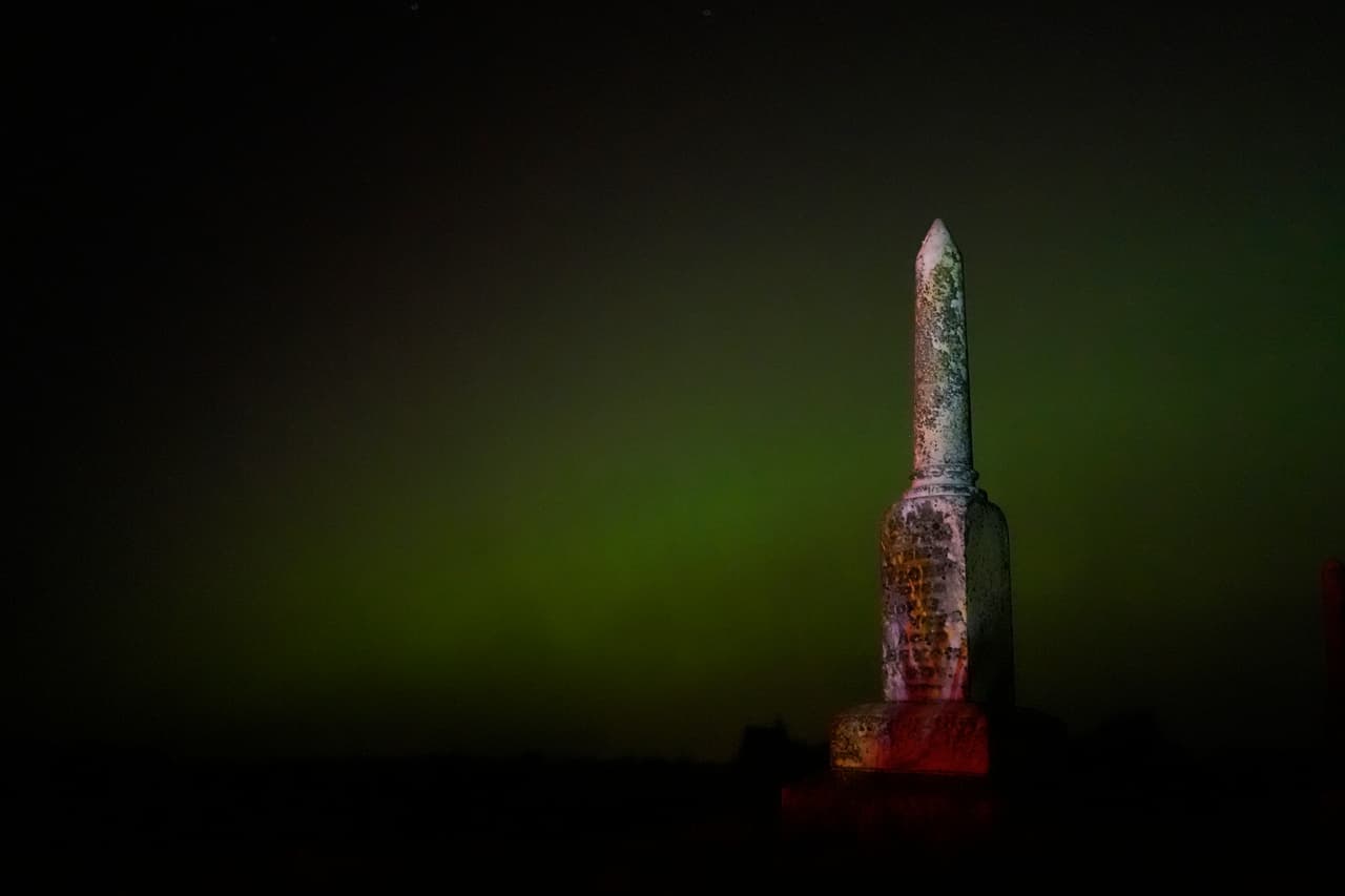 Una vieja lápida y detrás, la aurora boreal en un cementerio, cerca de Skidmore, Missouri.
