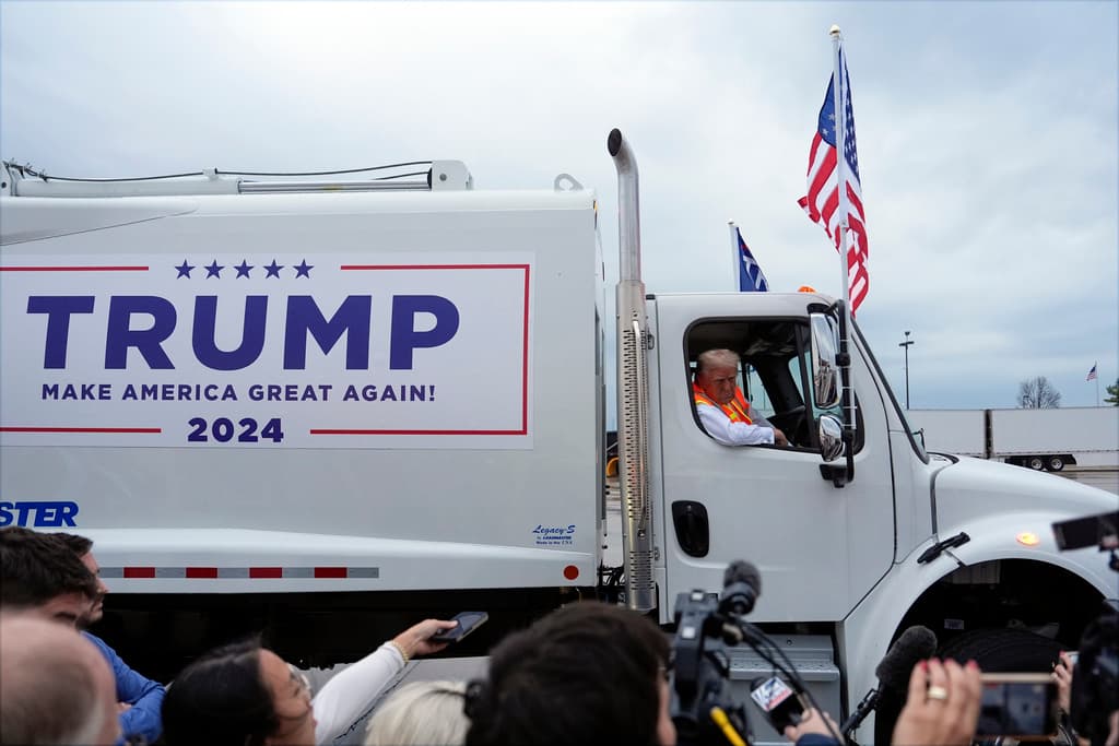 Trump montado en un camión de basura con el slogan de su campaña.