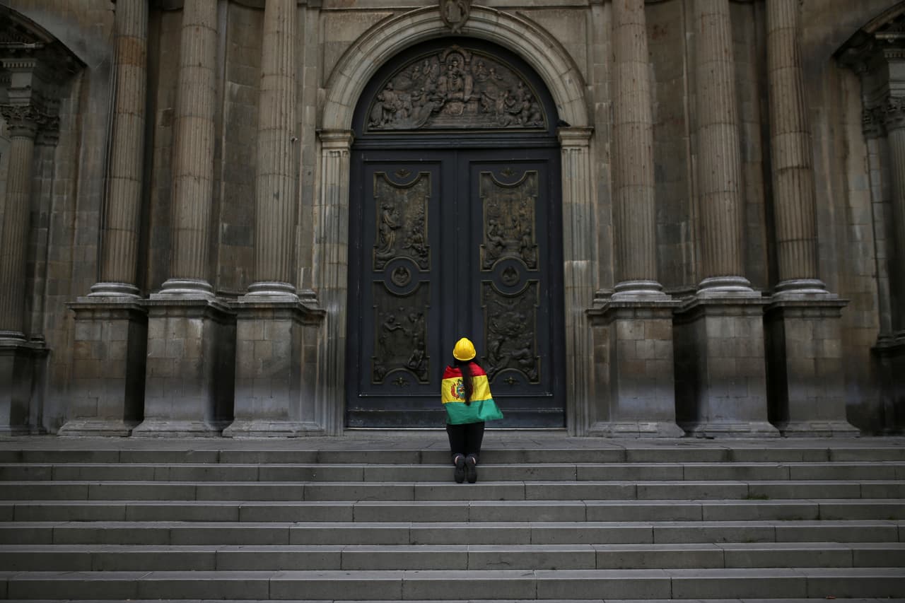 Arropada por una bandera, una boliviana reza frente a la Catedral de La Paz luego de que Morales informó su renuncia.
