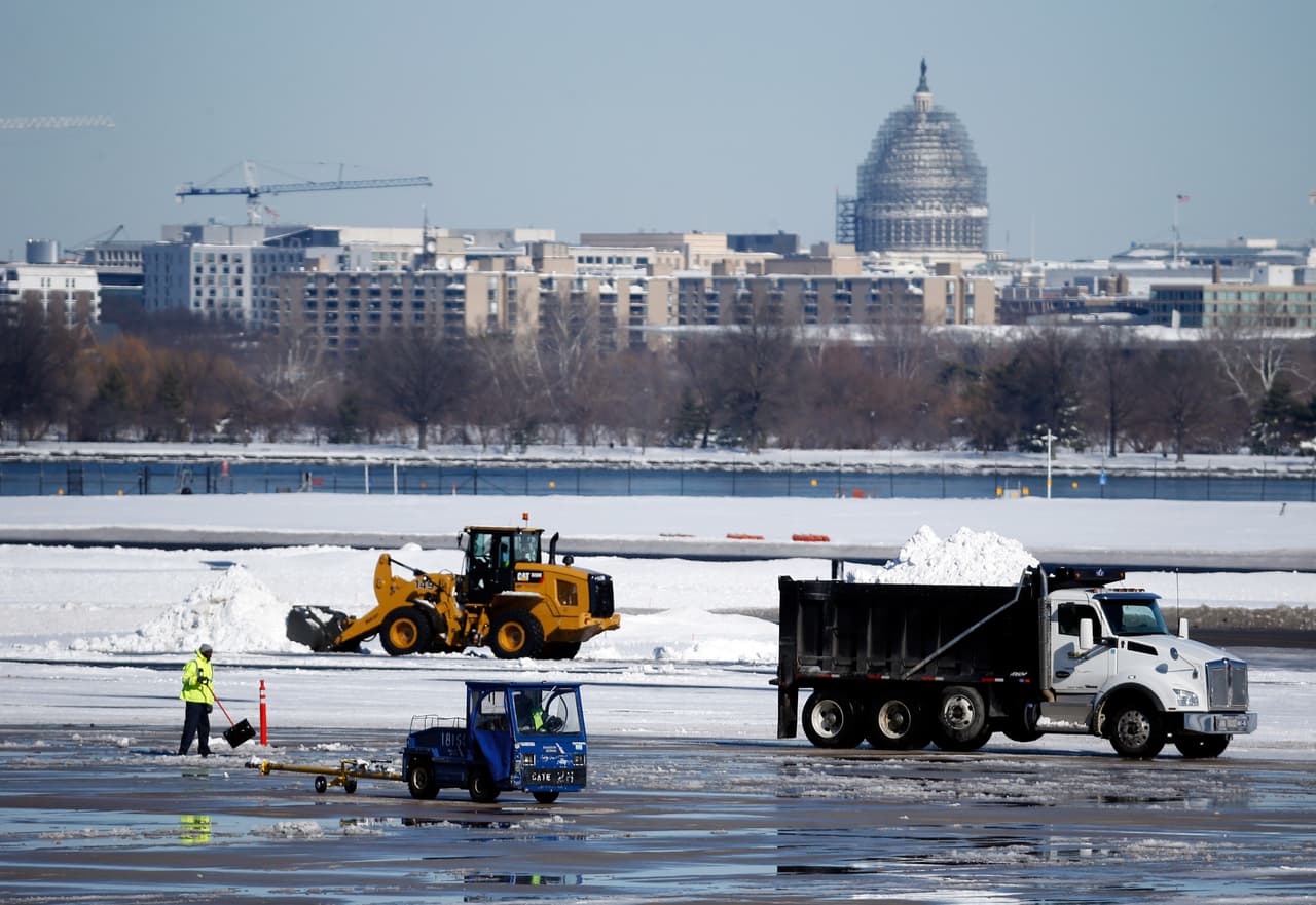 Trabajadores retiran la nieve de la pista en el aeropuerto nacional Ronald Reagan, en Arlington, Virginia, cercano a Washington, el domingo 24 de enero de 2016. Al fondo se aprecia el domo del capitolio en Washington. Millones de estadounidenses comenzaron el domingo a recuperarse de la gigantesca tormenta invernal debido a la cual cayó nieve sin precedente en un solo día en Washington y la ciudad de Nueva York. (AP Foto/Alex Brandon)