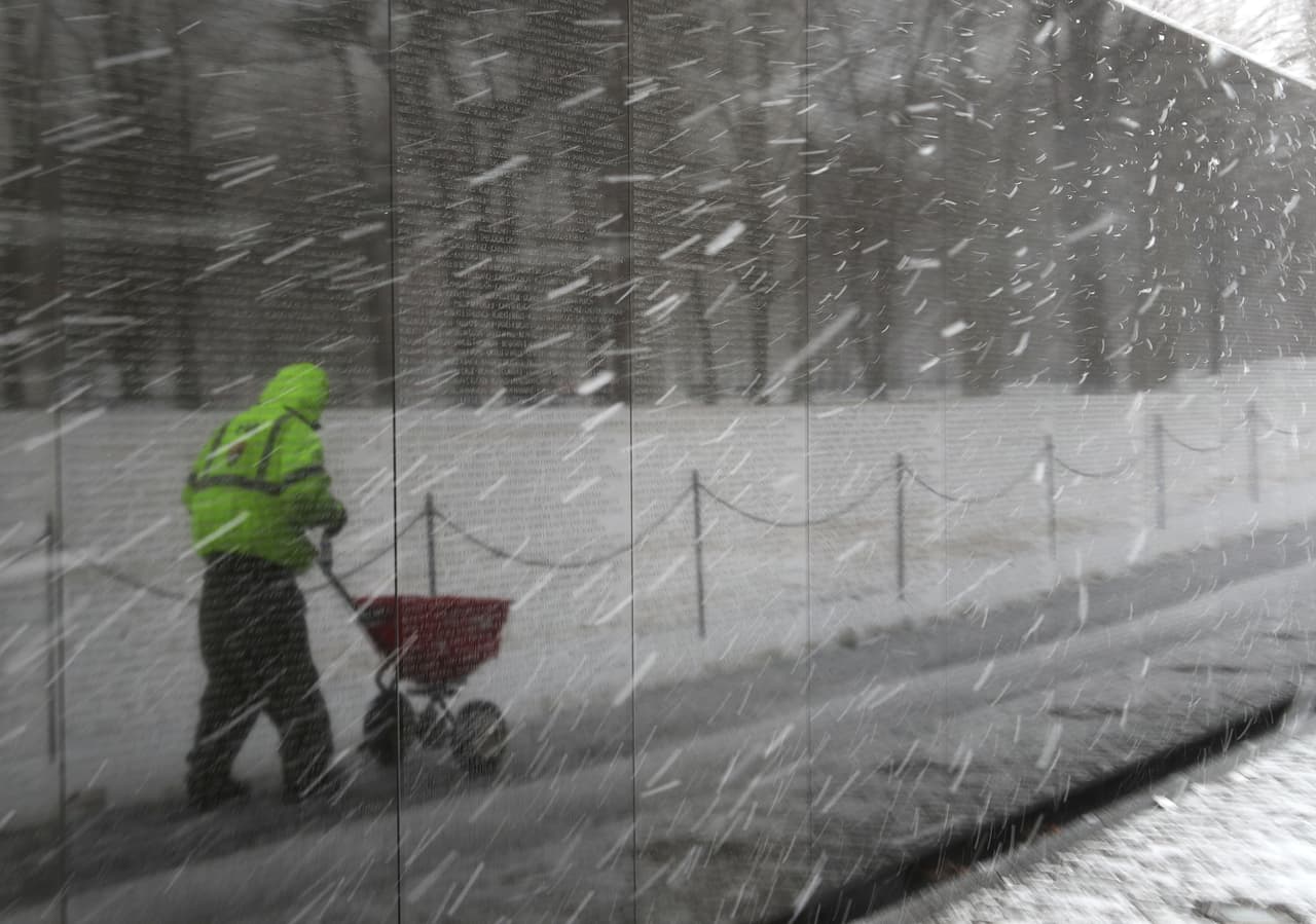 El monumento a los caídos en la Guerra de Vietnam en Washington DC. Un trabajador de servicio en Parques Nacionales tira sal en el suelo para ayudar a disolver las capas de nieve.
