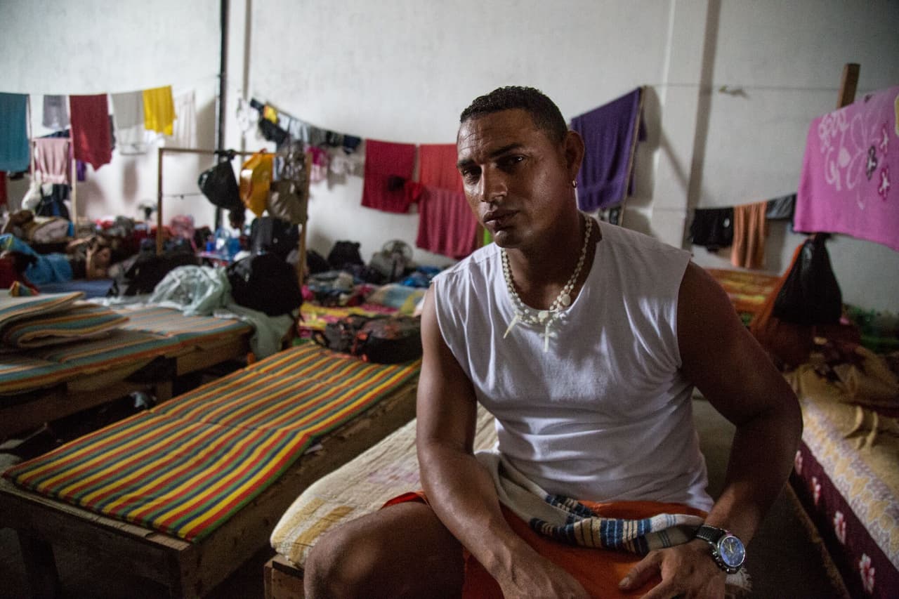 Reidiel Rodríguez sentado en su catre en el albergue. Cuenta que allí todo funciona con voluntariado. Los inmigrantes se presentan para limpiar los baños, preparar la comida y mantener el espacio. Él, como todos, busca un mejor futuro para su familia, algo que, asegura, ya era imposible en Cuba. Rodríguez cuenta que emigró de su isla porque perdió la esperanza de que las cosas mejoraran cuando vio la reacción negativa de los Castro por la reciente visita de presidente Barack Obama.
<br>