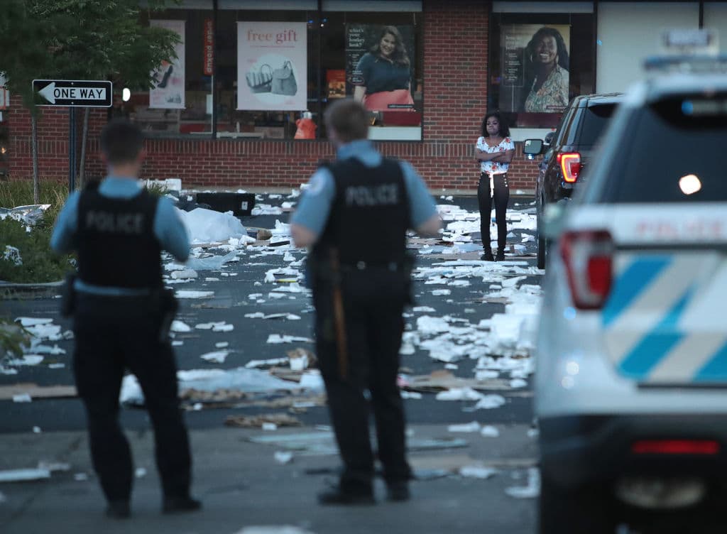 Una persona cerca de una tienda saqueada frente a oficiales de Policía. 
<br>