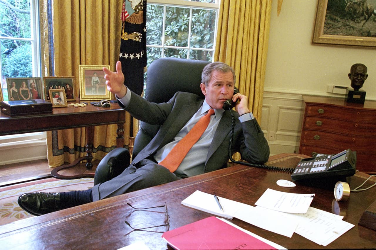 El despacho presidencial es un cuarto sin esquinas con vista al jardín. El presidente George W. Bush recibe un reporte telefónico en su escritorio de la Oficina Oval, 2001.