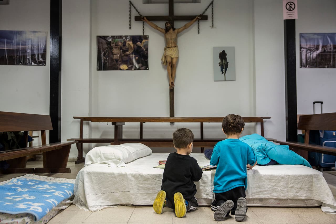 Dos niños, uno de familia georgiana y otro de familia colombiana, juegan en uno de los colchones puestos en la parroquia San Carlos Borromeo para atender a las familias solicitantes de asilo desatendidas por las instituciones.