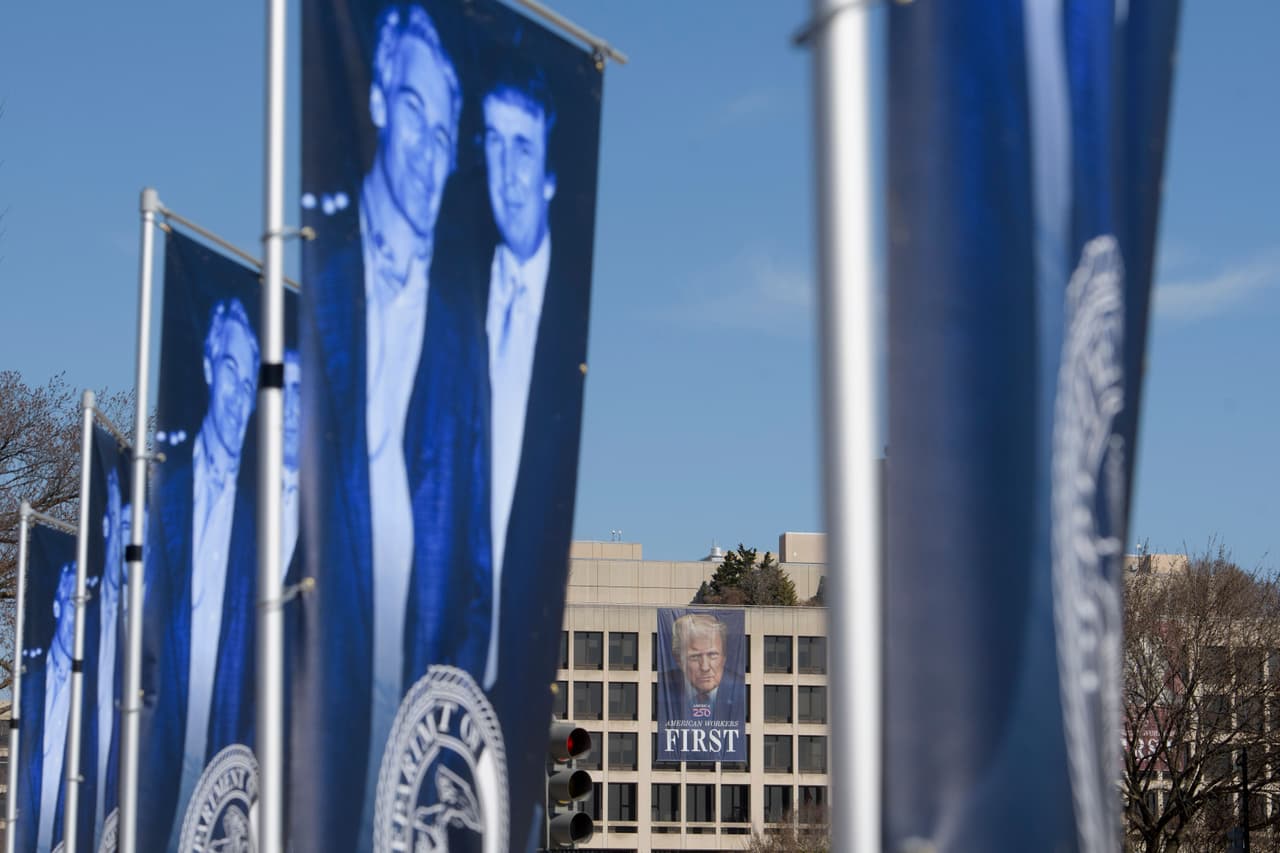 Una pancarta del presidente Donald Trump cuelga a lo lejos en el edificio del Departamento de Trabajo de EE. UU., mientras que pancartas que representan al presidente Donald Trump y a Jeffrey Epstein se ven en el National Mall.