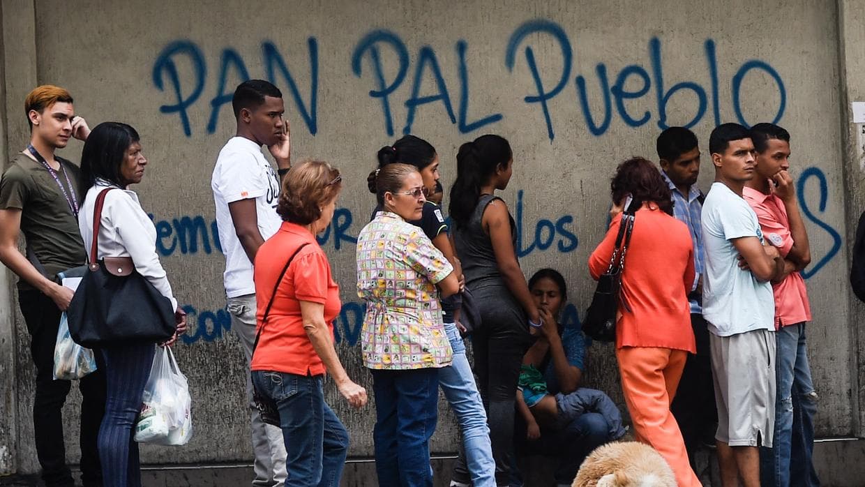 "Pan para el Pueblo" (Bread for the People) is written on the wall where a line of people waits for scarce food in Caracas. The Venezuelan government has confiscated private bakeries to ensure its supporters are fed.