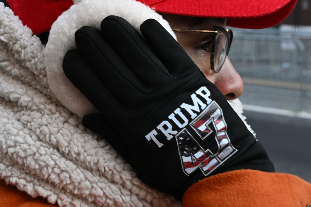 Un partidario del presidente estadounidense Donald Trump 
<b>usa unos guantes conmemorativos mientras soporta el frío para ver su caravana </b>mientras se dirige al Capitol One Arena.