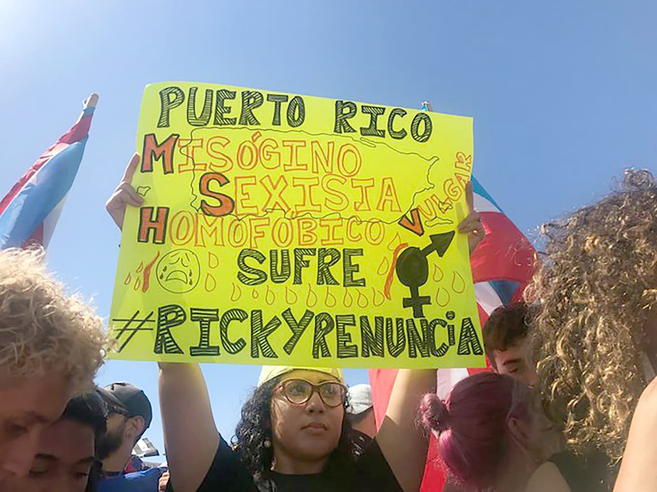 Carteles con mensajes que califican a Rosselló de misógino, sexista y homofóbico se ven en la manifestación de la capital de la isla. La Legislatura de Puerto Rico evaluará el contenido del chat y recomendará si procede activar por primera vez en la historia de la isla un mecanismo constitucional para sacarlo del poder.